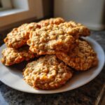 A close-up stack of golden brown banana oatmeal cookies on a white plate, catching the sunlight.