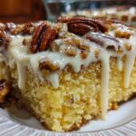 A moist slice of butter pecan praline poke cake topped with thick white glaze and whole pecans.