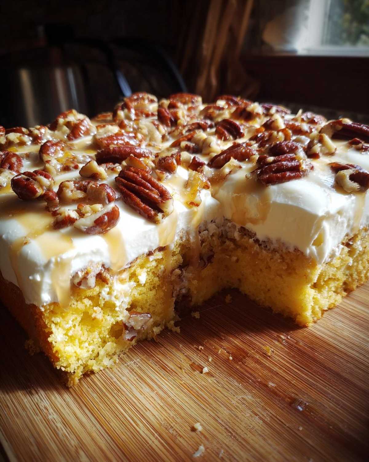 A close-up view of a section of butter pecan praline poke cake with a slice removed, showing the moist cake base, white frosting, and pecan topping.