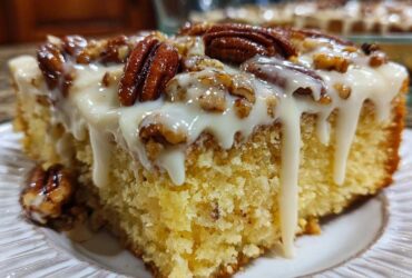 A moist slice of butter pecan praline poke cake topped with thick white glaze and whole pecans.