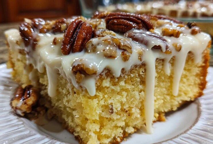 A moist slice of butter pecan praline poke cake topped with thick white glaze and whole pecans.