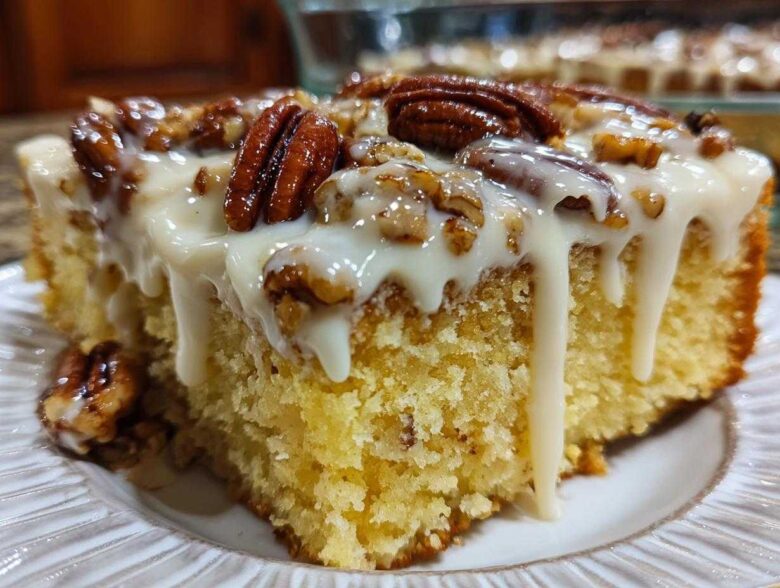 A moist slice of butter pecan praline poke cake topped with thick white glaze and whole pecans.