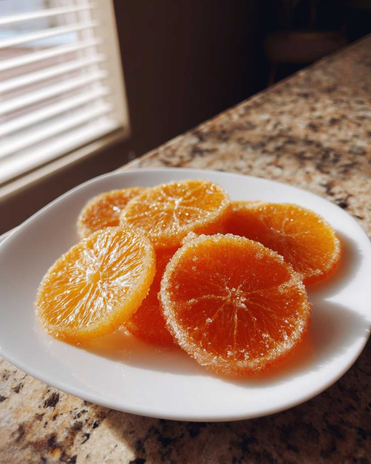 Five glistening candied orange slices dusted with sugar resting on a white plate.