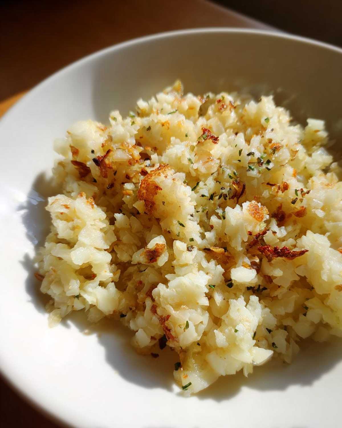 Close-up of fluffy, lightly browned cauliflower rice garnished with herbs in a white bowl.