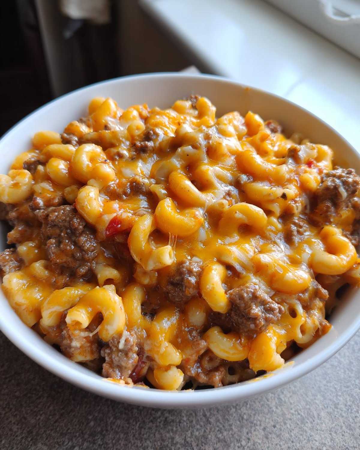 Close-up of a bowl filled with cheesy cheeseburger casserole, featuring elbow macaroni, ground beef, and melted cheddar cheese.