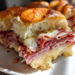 Close-up of a cheesy, baked grinder slider filled with layers of deli meat and melted provolone cheese.