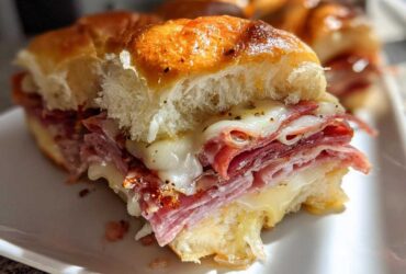 Close-up of a cheesy, baked grinder slider filled with layers of deli meat and melted provolone cheese.
