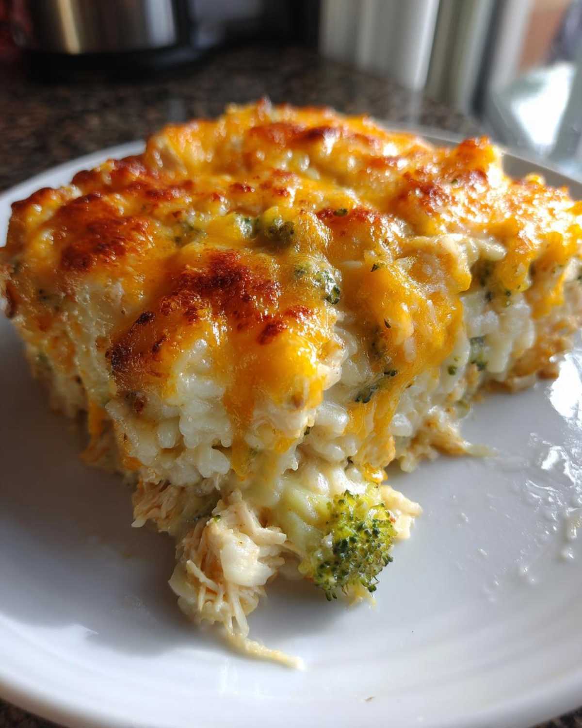 A close-up of a serving of cheesy rice casserole with broccoli and shredded chicken, featuring a browned cheese topping.