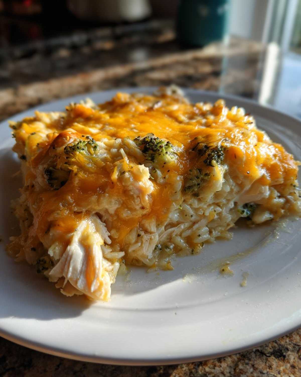 A close-up serving of creamy chicken and broccoli rice casserole topped with melted cheddar cheese.