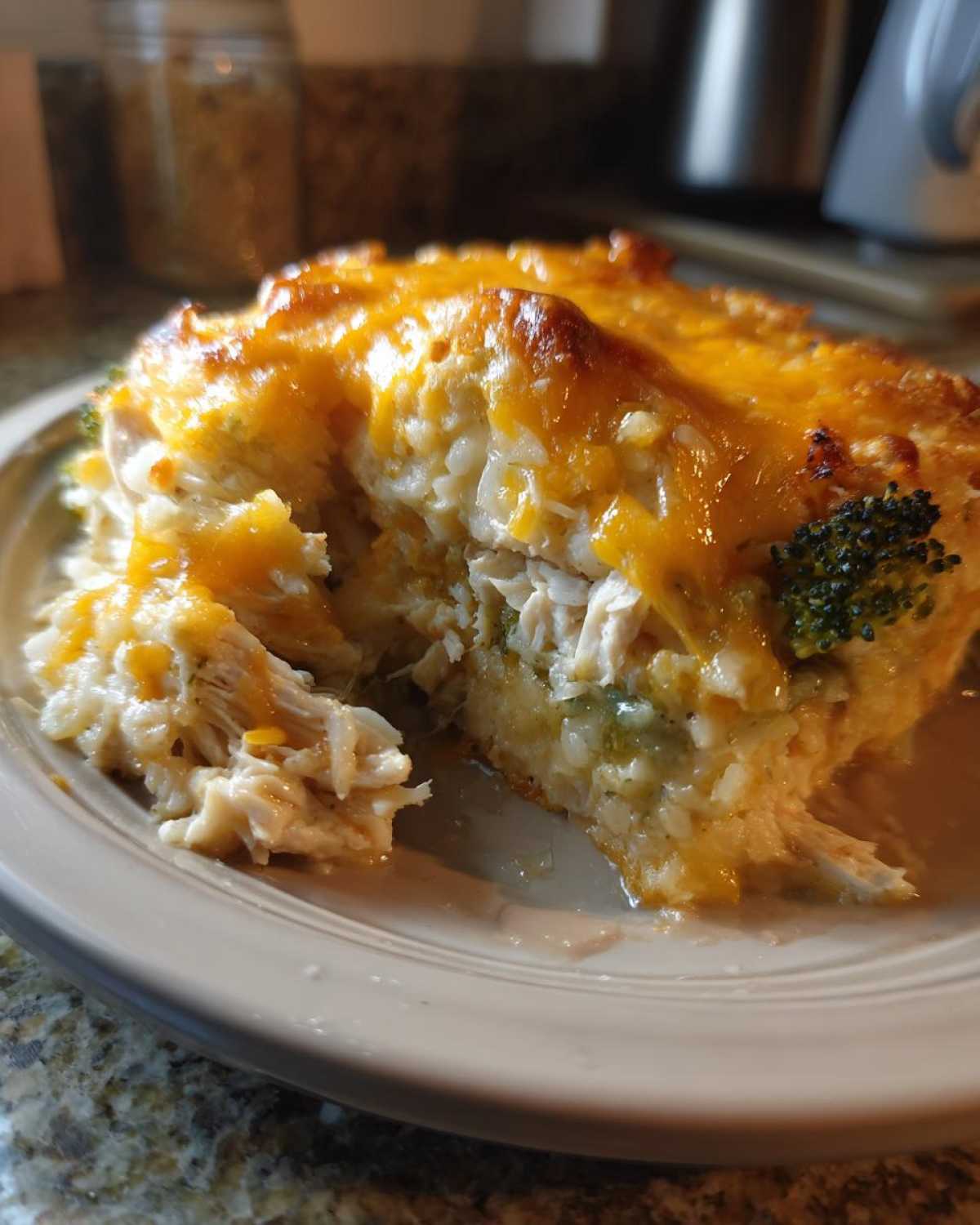 Close-up of a serving of creamy chicken and broccoli rice casserole topped with melted cheddar cheese.