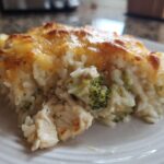 Close-up of a serving of creamy rice casserole mixed with chicken and broccoli, topped with melted, golden-brown cheese.