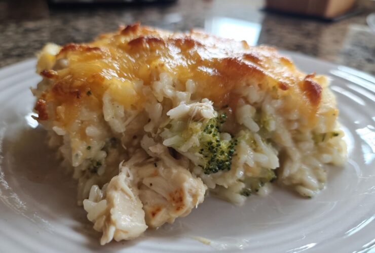 Close-up of a serving of creamy rice casserole mixed with chicken and broccoli, topped with melted, golden-brown cheese.
