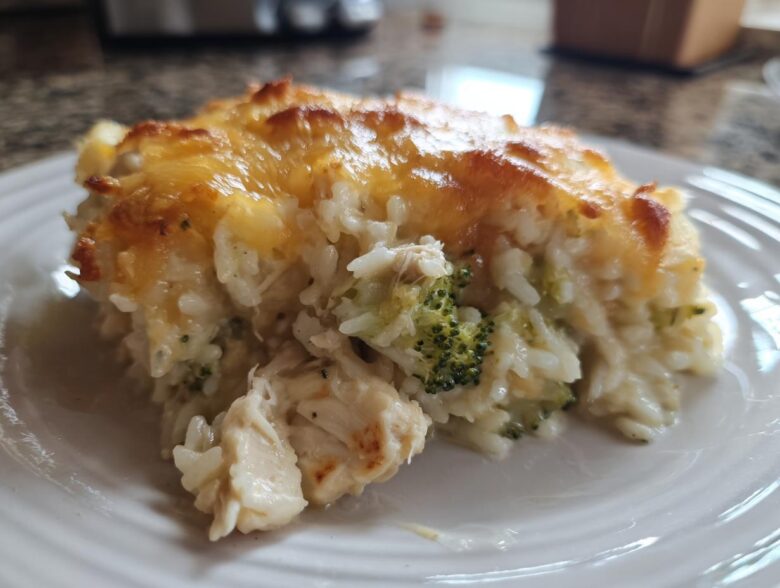 Close-up of a serving of creamy rice casserole mixed with chicken and broccoli, topped with melted, golden-brown cheese.