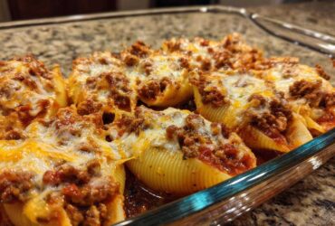 Close-up of baked stuffed shells topped with meat sauce and melted cheese in a clear glass baking dish.