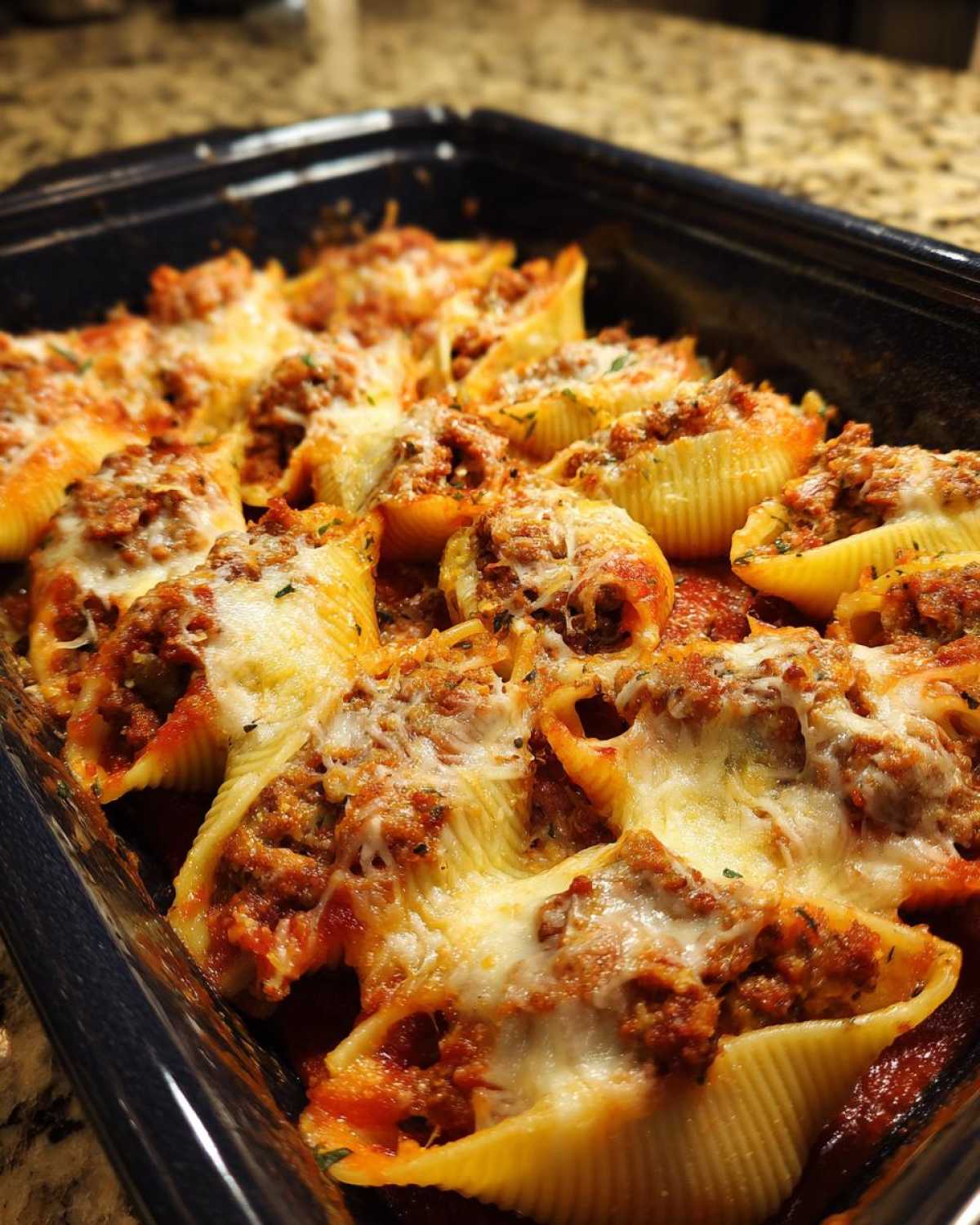 Close-up of baked stuffed shells overflowing with meat sauce and melted mozzarella cheese in a dark blue baking dish.