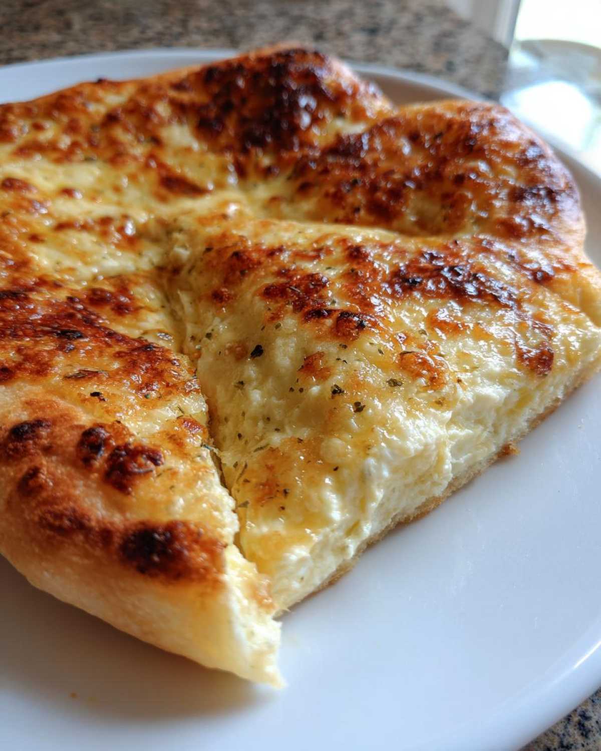 A close-up view of a thick slice of cheesy white pizza showing the creamy ricotta and browned mozzarella topping.