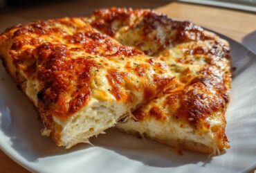 Two thick slices of white pizza with a bubbly, browned cheese topping resting on a white plate.