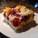 Close-up of a square slice of cherry dump cake with a golden crumb topping served on a white plate.