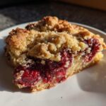 Close-up of a warm slice of cherry dump cake with a crumbly topping on a white plate.