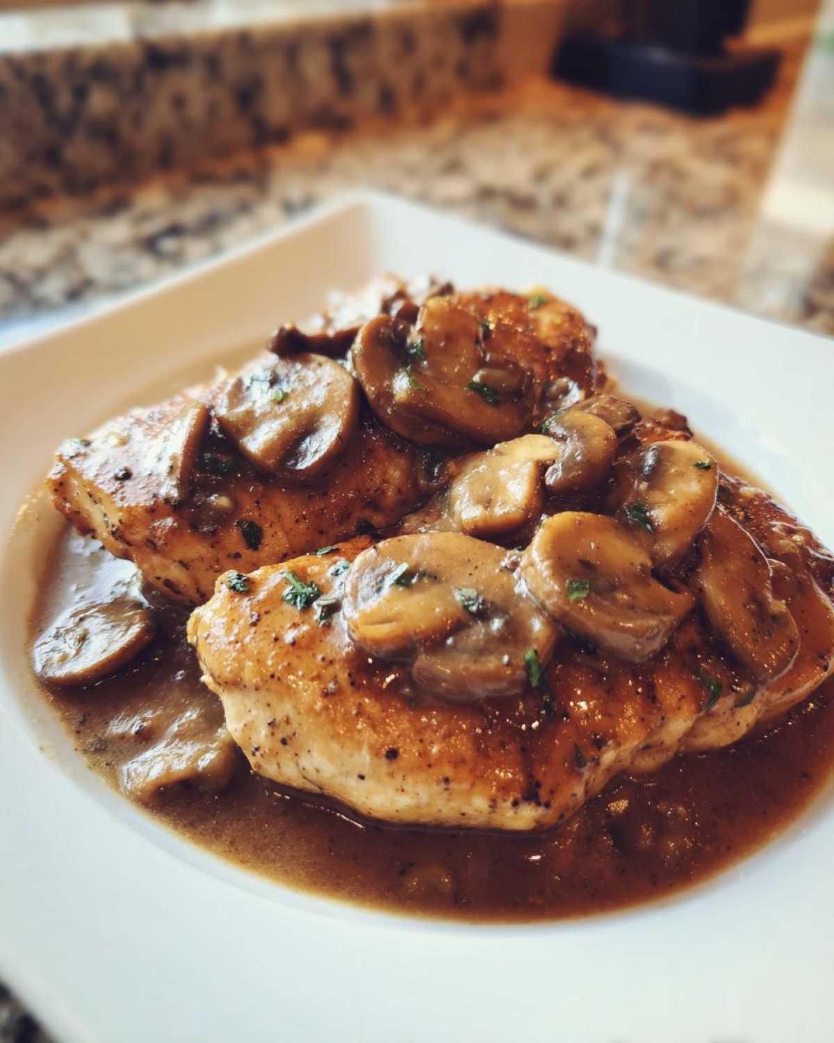 Close-up of two seasoned chicken breasts smothered in rich brown sauce and sliced mushrooms, classic chicken marsala.