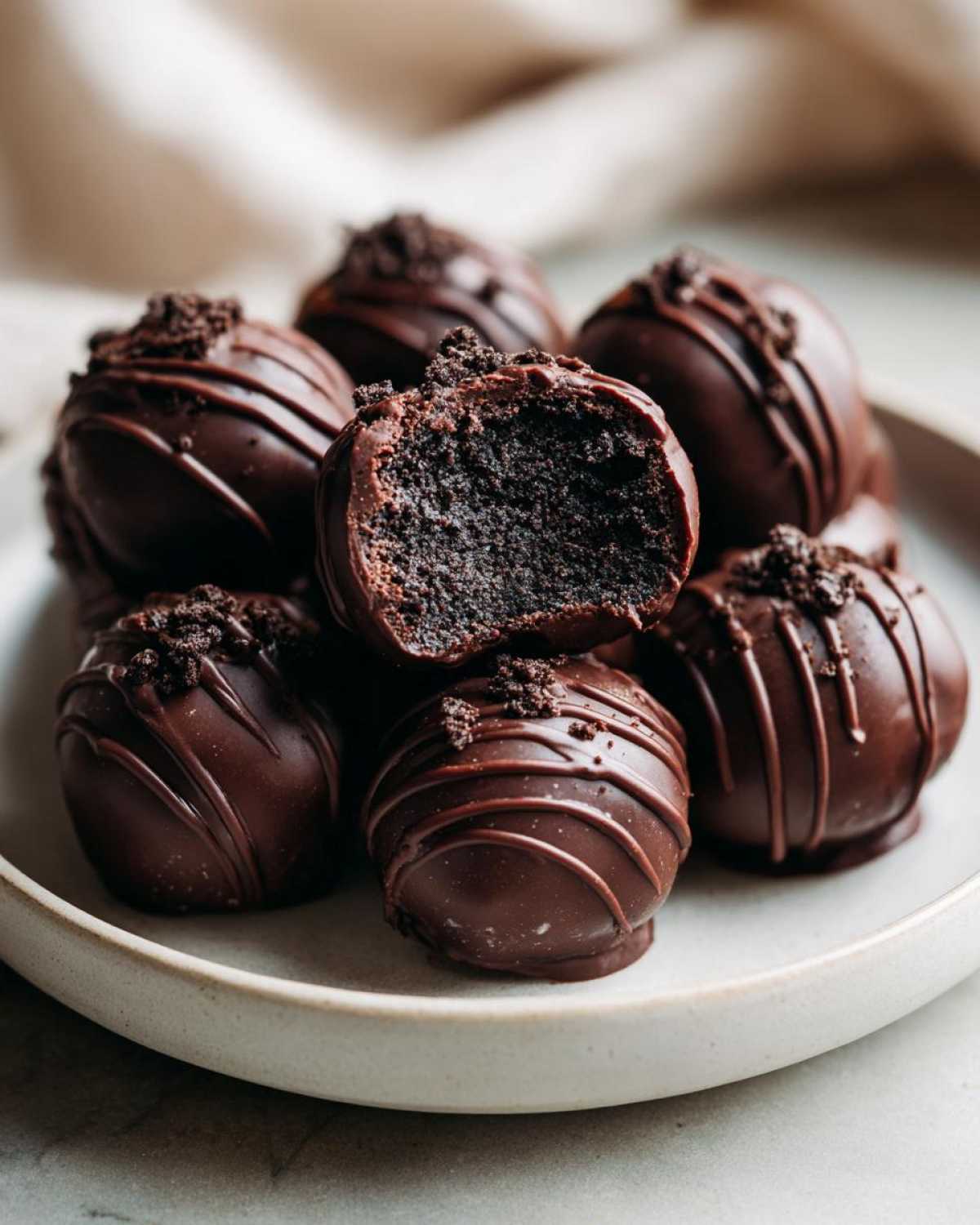 A plate of decadent chocolate-dipped Oreo balls, one cut open to show the dark, rich interior.