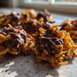 Close-up of two freshly made haystack cookies topped with melted chocolate, sitting on a counter.