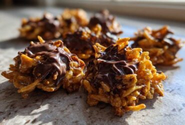Close-up of two freshly made haystack cookies topped with melted chocolate, sitting on a counter.
