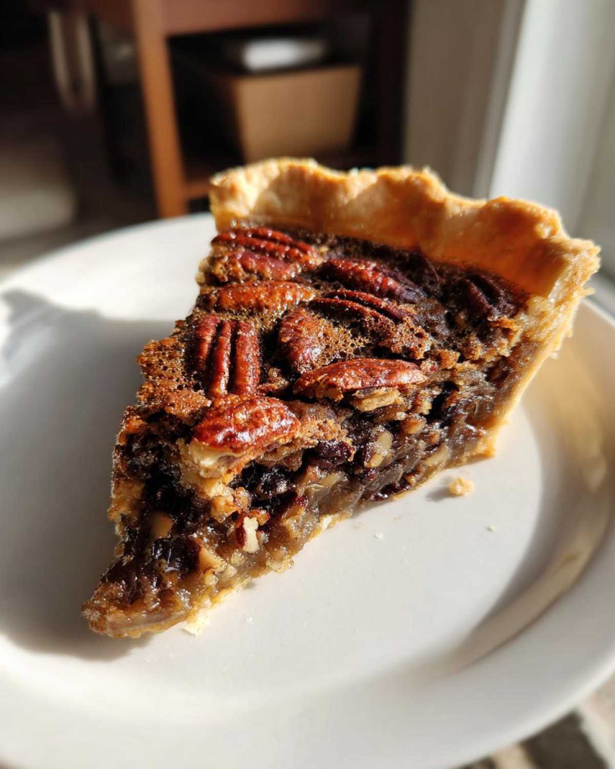 A close-up slice of rich chocolate pecan pie with a flaky crust, sitting on a white plate.
