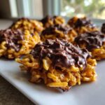 Close-up of several golden haystack cookies topped with melted dark chocolate served on a white plate.