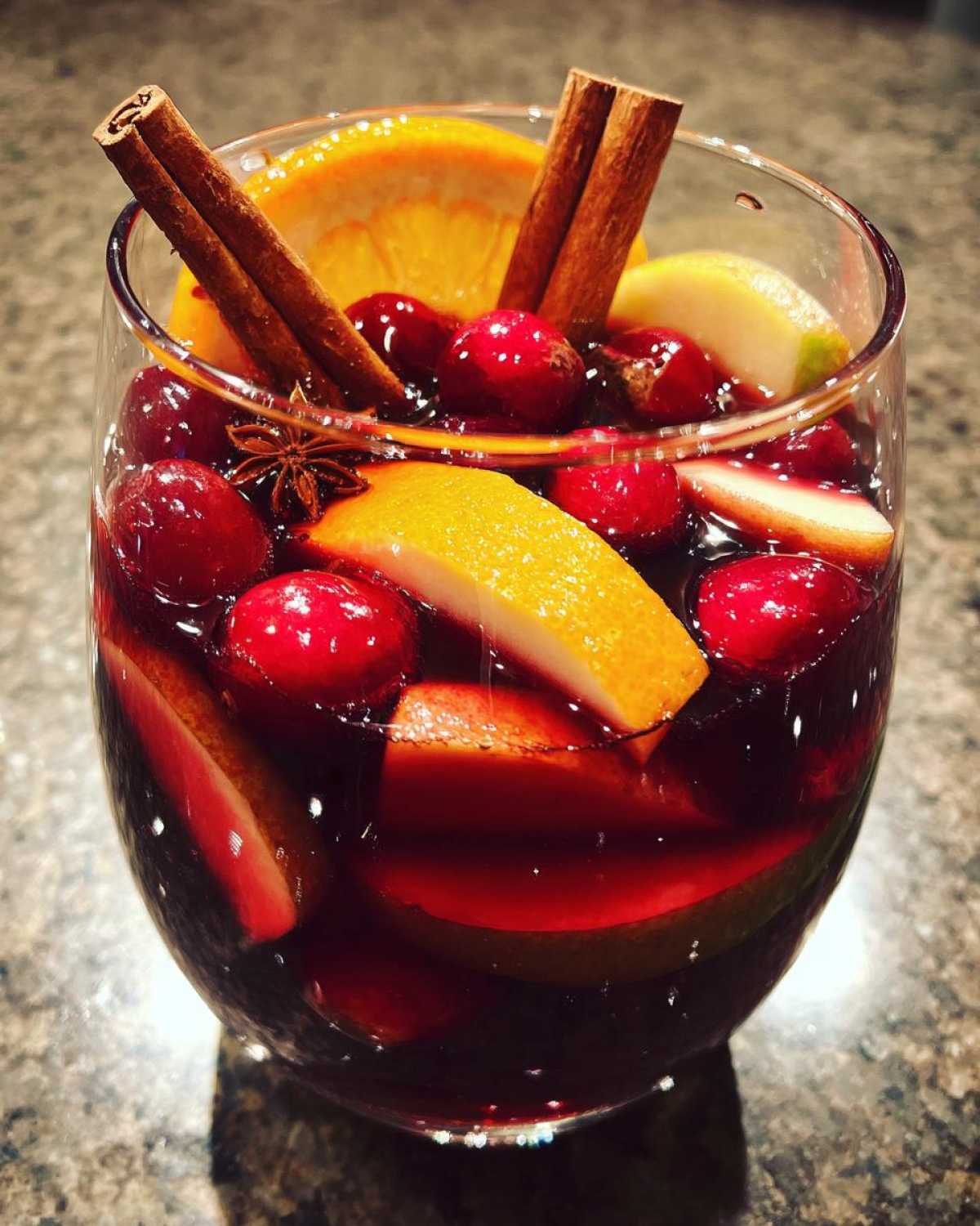Close-up of a glass filled with rich red christmas sangria, loaded with cranberries, orange slices, and cinnamon sticks.