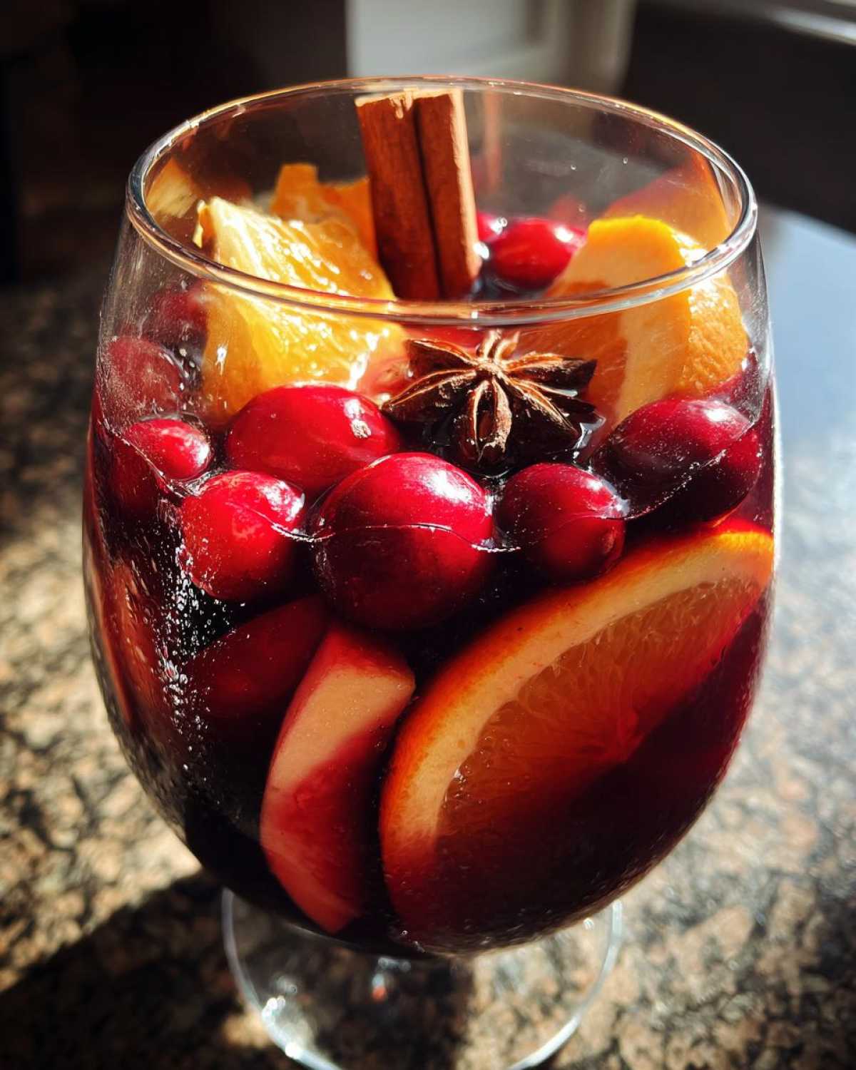 Close-up of a glass filled with rich red Christmas sangria, loaded with cranberries, orange slices, and spices like star anise and cinnamon.