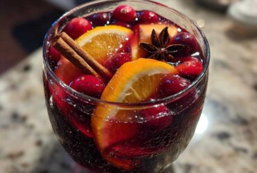 Close-up of a glass filled with vibrant red christmas sangria, garnished with orange slices, cranberries, cinnamon sticks, and star anise.