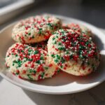 A close-up of four soft, round christmas sprinkle sugar cookies covered in red, green, and white nonpareils.