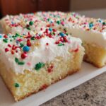 Two slices of soft christmas sugar cookie bars topped with thick white frosting and colorful holiday sprinkles.