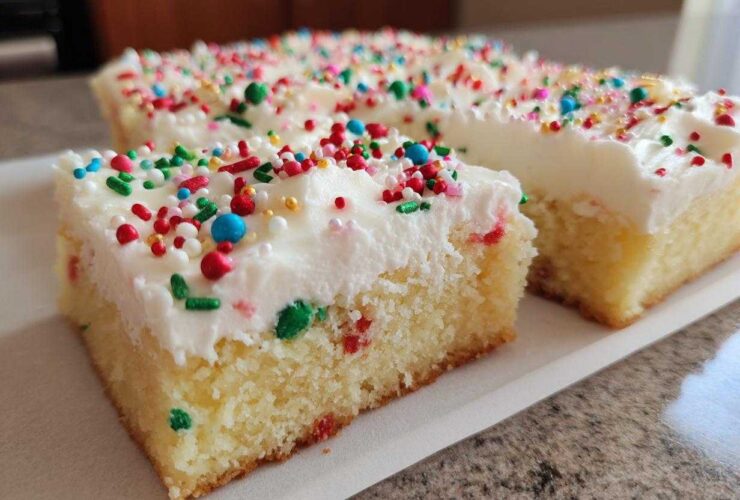Two slices of soft christmas sugar cookie bars topped with thick white frosting and colorful holiday sprinkles.