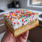 Close-up of a square slice of christmas sugar cookie bars topped with thick white frosting and colorful sprinkles.