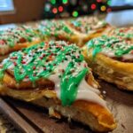Close-up of freshly baked christmas tree cinnamon rolls topped with white and green icing and festive sprinkles.