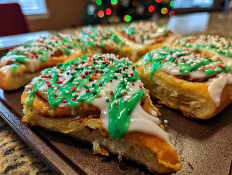 Close-up of freshly baked christmas tree cinnamon rolls topped with white and green icing and festive sprinkles.