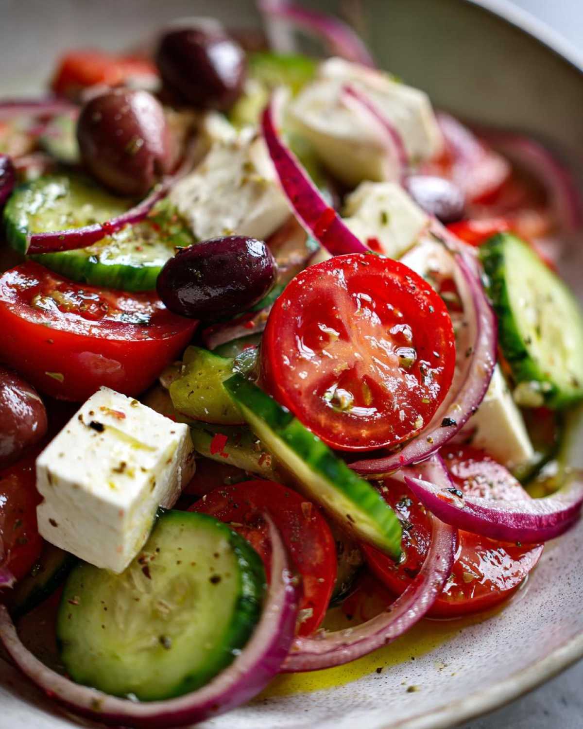 Close-up, vibrant photo of a fresh greek salad featuring tomatoes, cucumbers, feta cheese, red onion, and Kalamata olives.