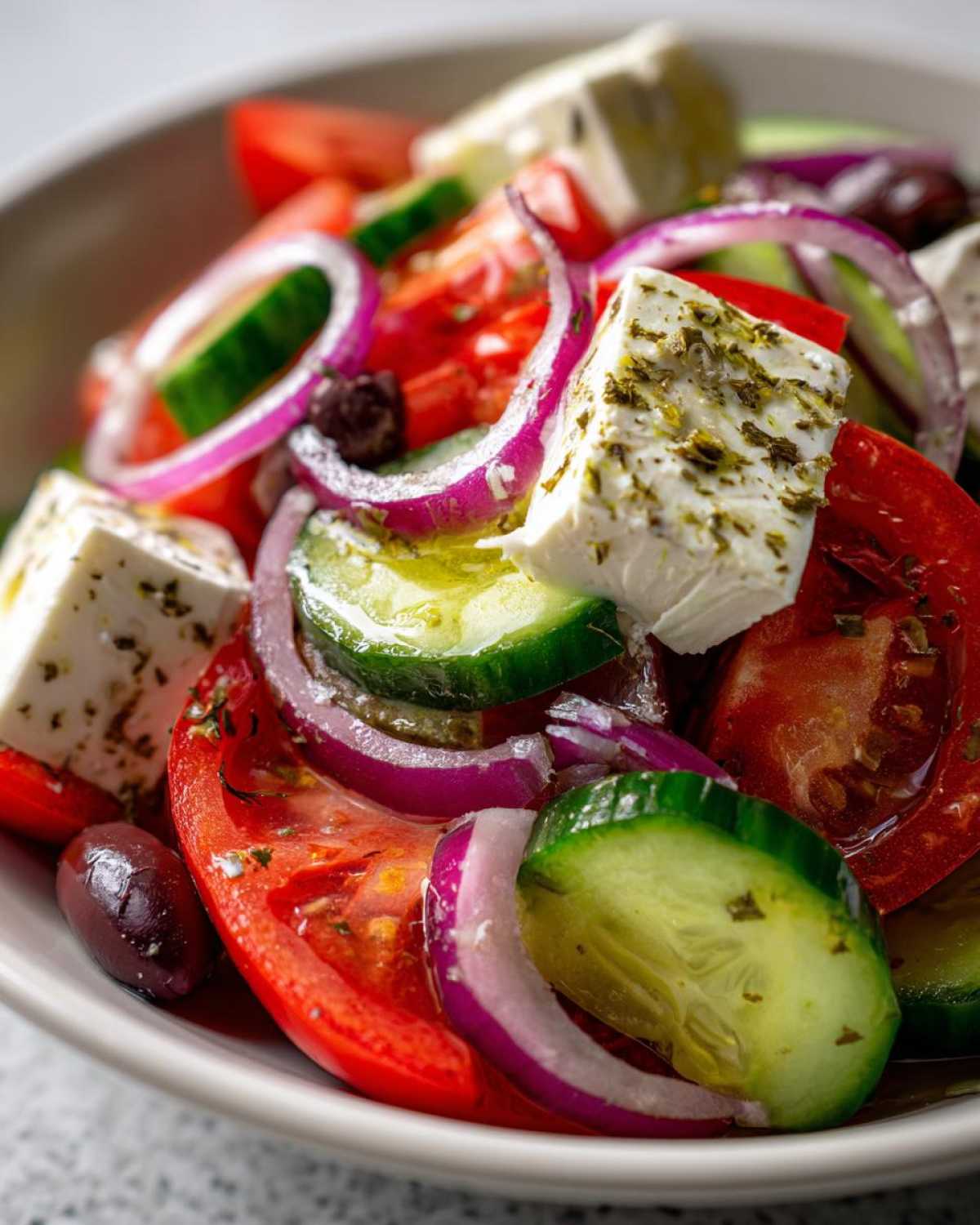 Close-up of a vibrant greek salad featuring chunks of feta cheese, red onion rings, cucumber slices, and Kalamata olives.