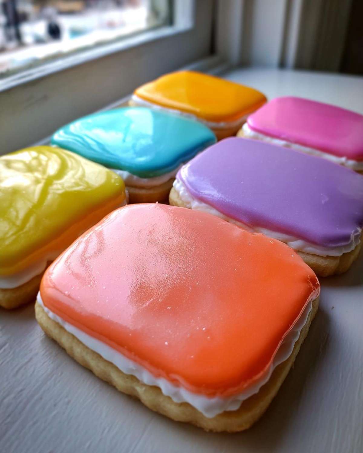 Rectangular sugar cookies topped with vibrant, glossy sugar cookie icing that hardens in orange, purple, blue, and yellow.
