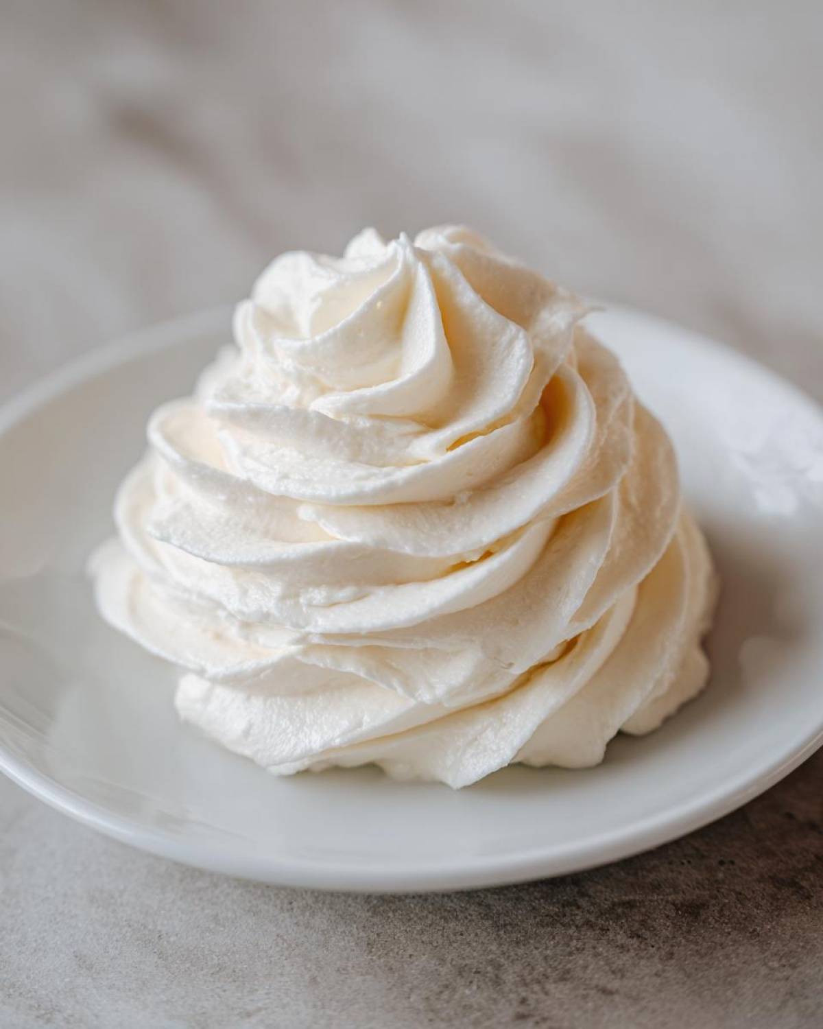 A perfectly piped swirl of fluffy white cream cheese frosting sitting on a small white plate.