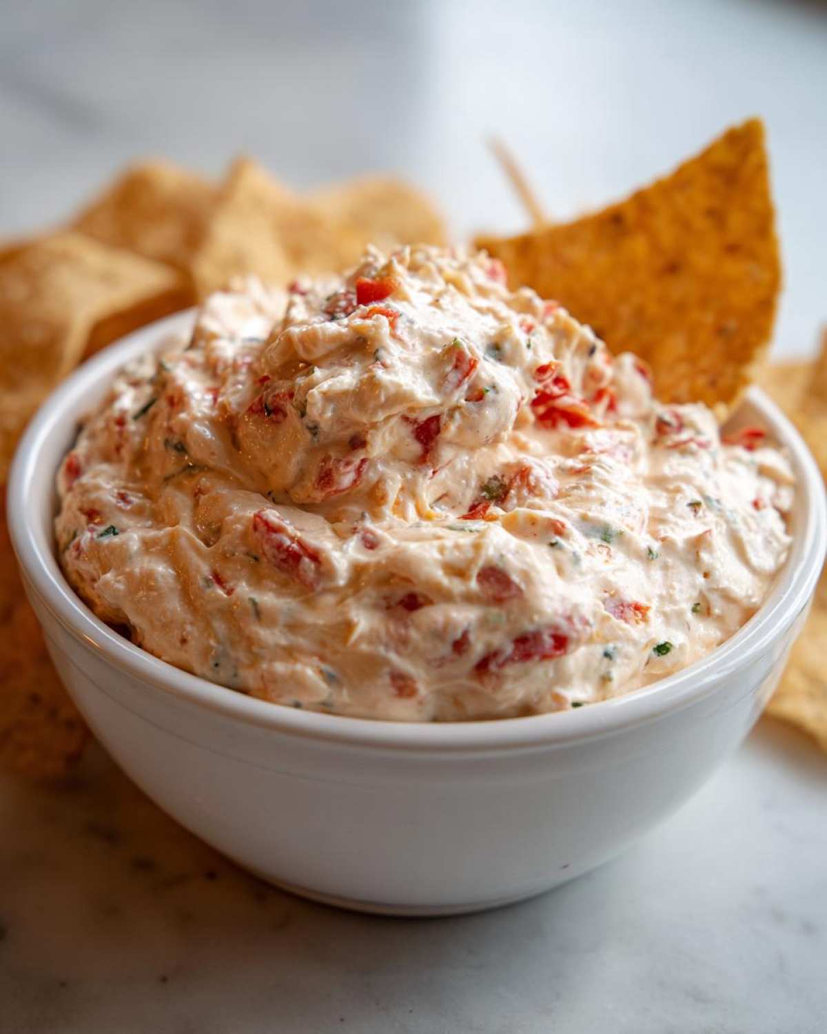 Close-up of creamy, chunky boat dip served in a white bowl with tortilla chips.