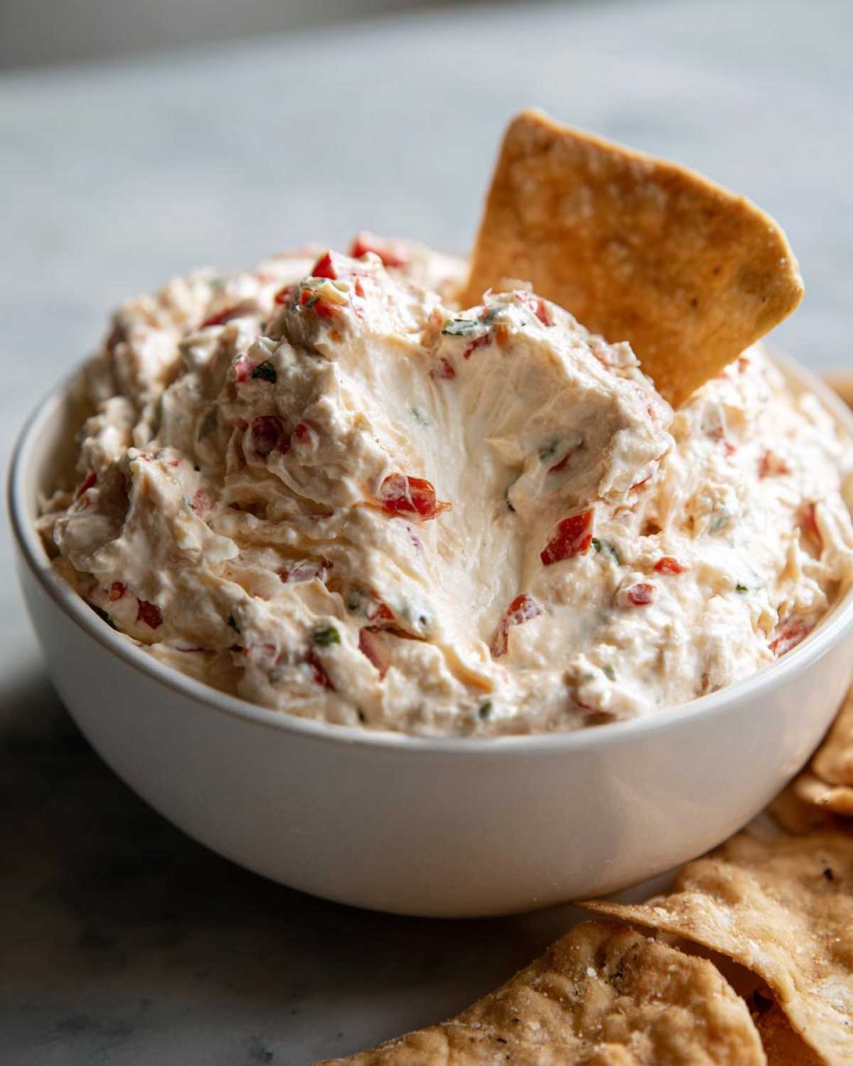 Close-up of creamy boat dip in a white bowl with a cracker dipped in.