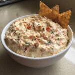 A white bowl filled with creamy, chunky boat dip, garnished with tortilla chips.