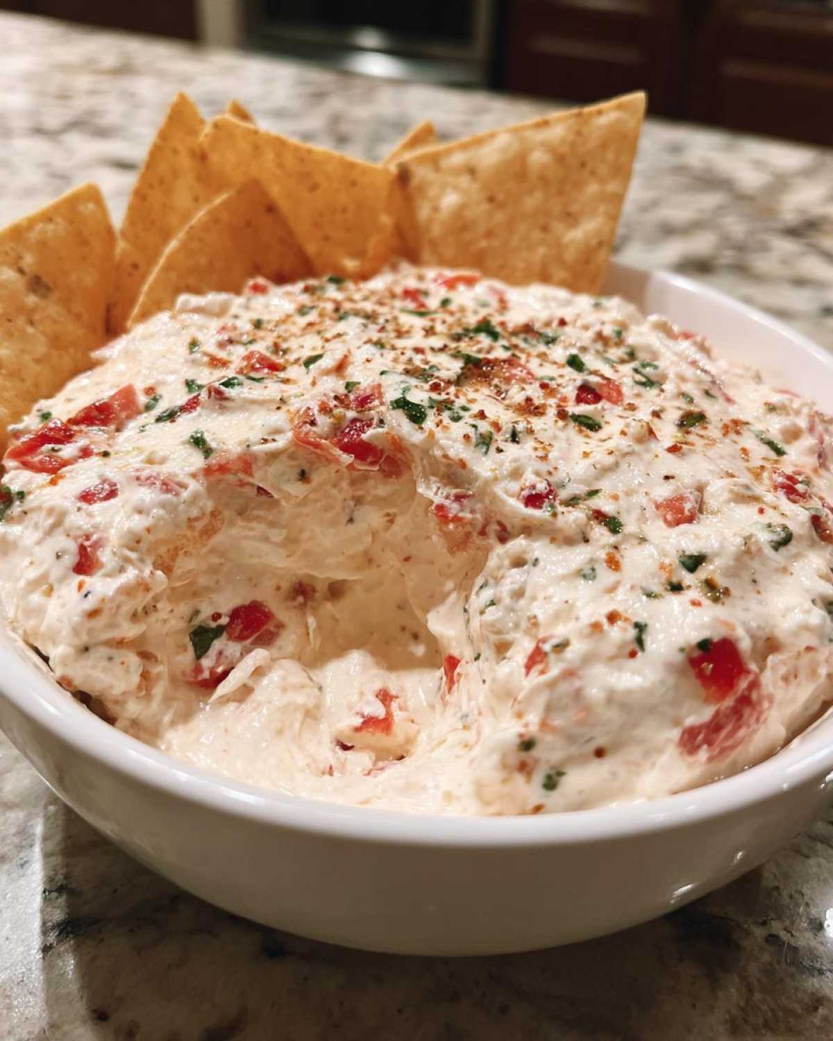 A close-up of creamy boat dip in a white bowl, topped with spices, served with tortilla chips for dipping.
