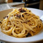 Close-up of creamy caramelized onion pasta tossed in a white bowl, topped with dark caramelized onions.