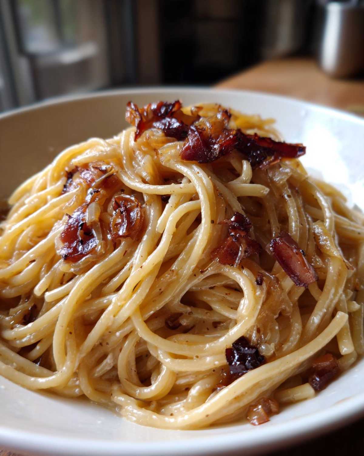 Close-up of creamy caramelized onion pasta served in a white bowl, topped with dark caramelized onions.