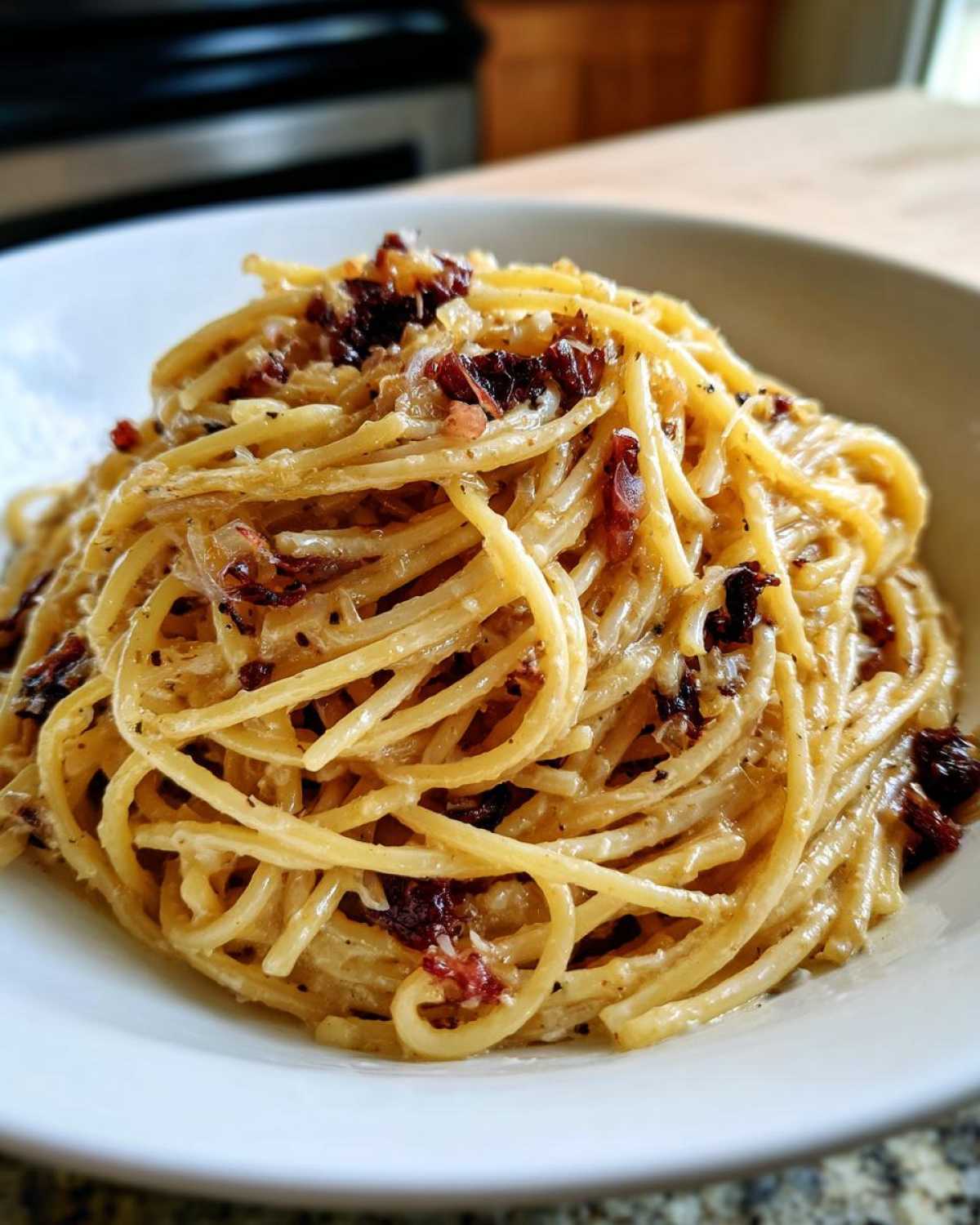 Close-up of creamy caramelized onion pasta (spaghetti) tossed with dark caramelized onions and cheese in a white bowl.