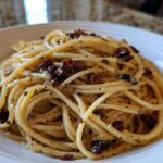 Close-up of creamy caramelized onion pasta tossed with herbs and dark bits of onion in a white bowl.